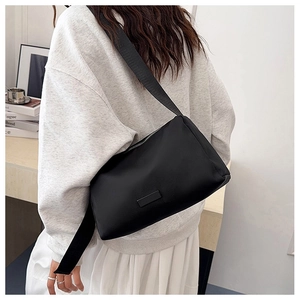 Detail of minimalist black nylon crossbody bag with wide shoulder strap worn by model