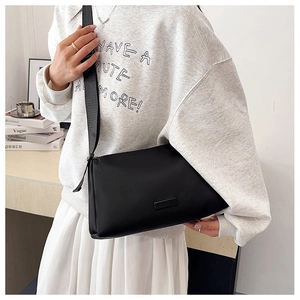Detail view of black minimalist crossbody bag with wide strap and logo plaque on model