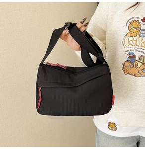 Detail of black nylon crossbody bag featuring a red zipper pull and a fashion side label