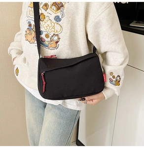 Detail view of black nylon crossbody bag featuring textured fabric and red fashion label