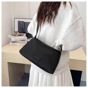 Detail of minimalist black nylon shoulder bag with zip closure on a lifestyle background