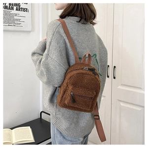 Dettaglio di un mini zaino in peluche marrone con chiusura a zip e spallacci in tessuto