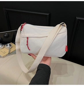 Detail of white nylon crossbody bag with textured fabric and red fashion label