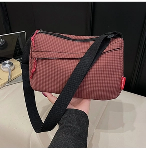 Detailed shot of red-brown checkered nylon crossbody bag with black strap and fashion label