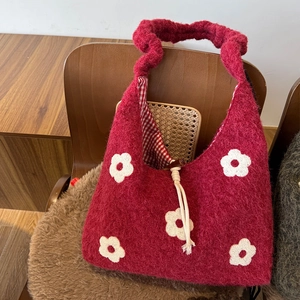 Close-up of wine red knit bag with white floral embroidery and checkered lining