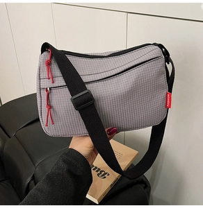Detail of grey plaid nylon crossbody bag with red fashion tag and zipper puller