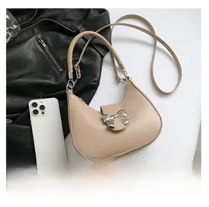 Detail of beige half-moon bag featuring silver bow hardware and leather shoulder strap
