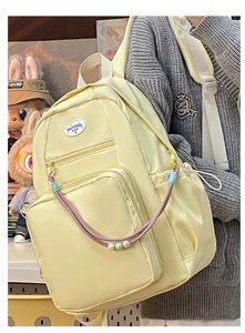 Dettaglio di uno zaino ita giallo pallido in nylon impermeabile con ciondoli colorati