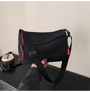 Detail view of black nylon crossbody bag with red fashion label and drawstring puller