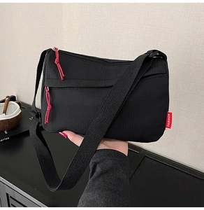 Close-up of black nylon crossbody bag featuring a red knot zipper and fashion tag