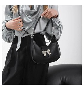Detail of black leather crescent handbag featuring a silver metal bow and round handle