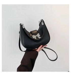Detail of silver metallic bow buckle on black matte leather crescent moon handbag