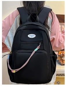 Dettaglio dello zaino in nylon nero con etichetta del logo e cordino intrecciato con perline
