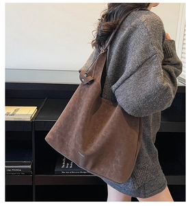 Detail view of dark brown suede tote bag featuring a silver logo and wide shoulder strap