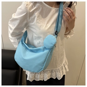 Close-up of a light blue nylon crescent crossbody bag with a round mini pouch on a model