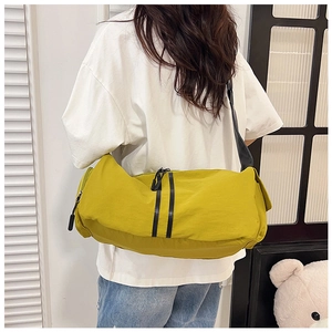 Detail of a mustard yellow nylon cylinder crossbody bag with black stripe accents and zipper