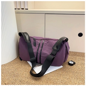 Detail of purple ruched nylon travel bag featuring black wide strap and zipper closure