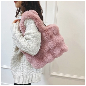 Détail d'un sac à main en peluche rose associé à un pull en maille blanche d'hiver