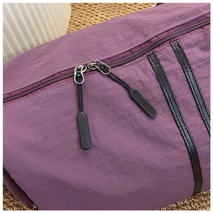 Detail of purple nylon travel bag showing dual metal zippers and black leather trim