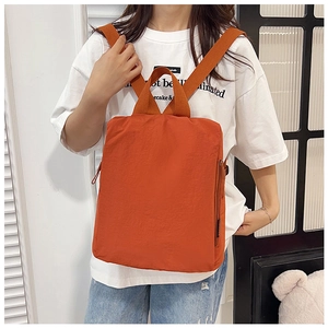 Detail of a bright orange nylon backpack with textured fabric and top handle on a model