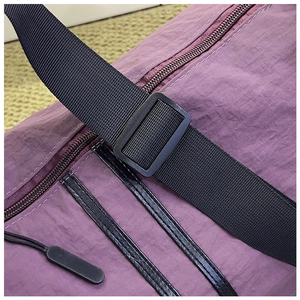 Detail of purple nylon travel bag showing black adjustable strap and zipper texture