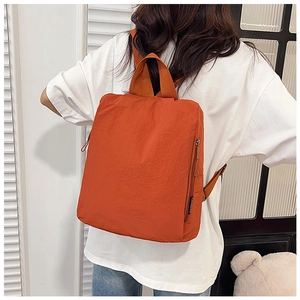 Rear view of a bright orange waterproof nylon backpack worn by a person near a window