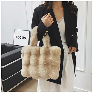 Détail d'un sac cabas en peluche beige avec texture matelassée bulles tenu par un mannequin