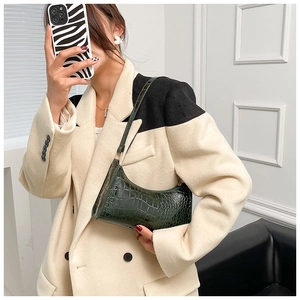 Detail view of dark green crocodile pattern shoulder bag on beige winter coat