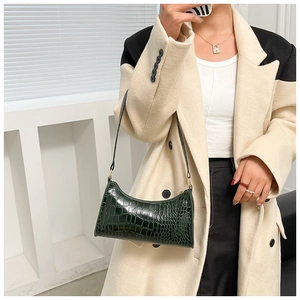 Detail of dark green crocodile texture baguette bag with glossy leather and gold zipper