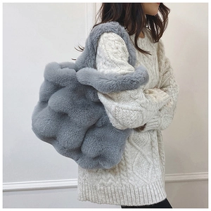 Sac fourre-tout gris en peluche porté par un mannequin en pull blanc dans un cadre cosy