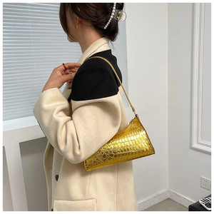 Close-up of golden metallic crocodile pattern baguette bag worn by model on shoulder