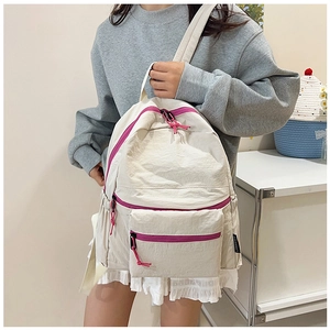 Detail view of cream white backpack with pink zippers and delicate white lace trim on bottom