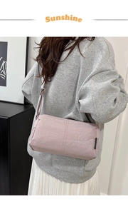 Detailed side view of light pink crossbody bag with adjustable strap on a model