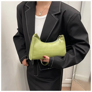 Detail shot of green crocodile-embossed crescent bag with golden zipper and animal texture