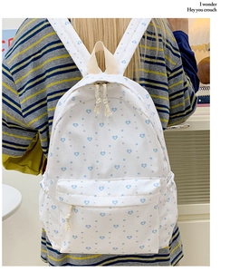 Detail of white canvas backpack with blue heart prints and woven rope zipper pull