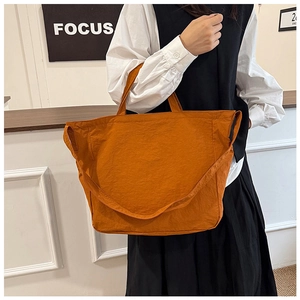 Detail view of the bright orange nylon tote bag showing textured fabric and wide shoulder strap