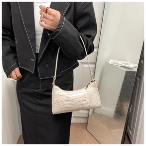 Detail view of cream baguette bag with crocodile pattern and golden zipper on shoulder