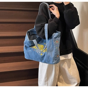 Sac cabas en jean délavé bleu avec broderie porté par un mannequin sur un escalier