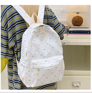 Detail of white canvas backpack with blue heart prints and woven zipper puller
