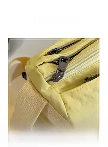 Detail of yellow nylon bag showing three smooth metal zippers and thick cream shoulder strap