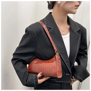 Detail view of a brown crocodile pattern baguette bag worn over a black blazer