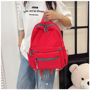 Detail of red water-resistant nylon backpack featuring contrast green zippers and pocket