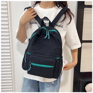 Detail of black nylon backpack with green zippers shown on a model in a casual setting