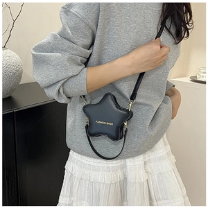 Star-shaped black crossbody bag with gold lettering shown on a model in casual outfit