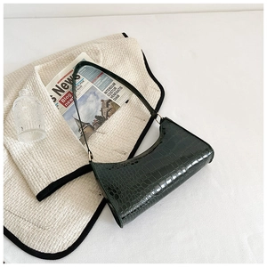 Green crocodile pattern baguette bag on white background with tweed and newspaper