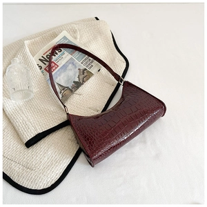 Detail shot of a dark burgundy crocodile textured baguette bag on a tweed jacket