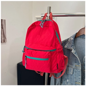Detail of red nylon backpack showing contrasting green zippers and multi-pocket design