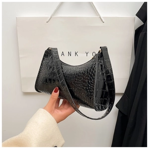 Detail of black faux crocodile skin handbag with glossy finish and curved baguette shape