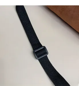 Detail view of adjustable black nylon strap with plastic buckle on brown suede bag