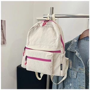 Detail view of cream nylon backpack featuring pink zippers and side brand label